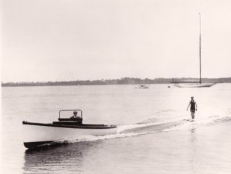 Image of man in an old fashioned swimsuit aquaplaning behind a small powerboat