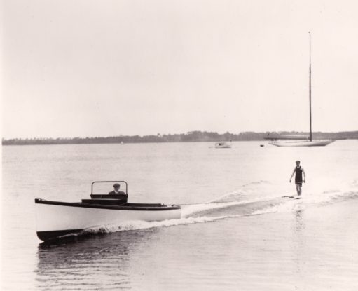 Image of man in an old fashioned swimsuit aquaplaning behind a small powerboat