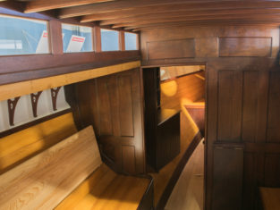 View of the catboat CLARA's cabin looking forward; glass rectangular windows along the upper left let lots of light into the cabin. You can see past a bulkhead into the forepeak..