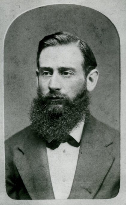 Black and white photo of young Nat Herreshoff, wearing a suit and bowtie, nicely combed hair and a full beard.