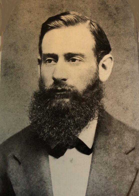 sepia tone photo of young Nat Herreshoff, wearing a suit and bowtie, nicely combed hair and a full beard.