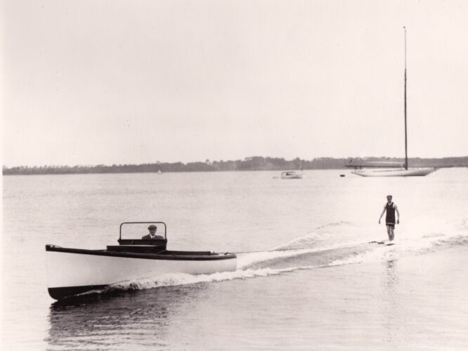 Image of man in an old fashioned swimsuit aquaplaning behind a small powerboat