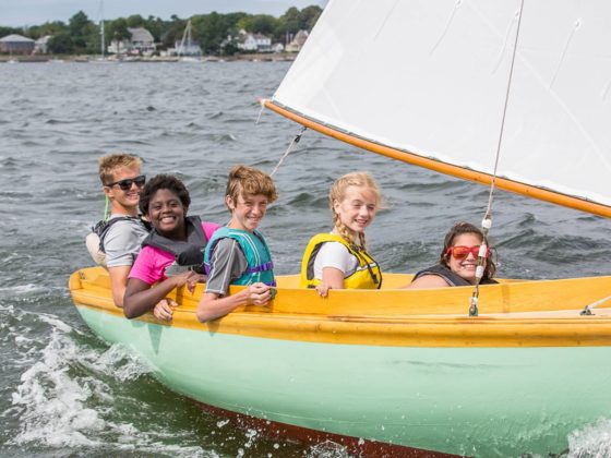 five smiling students on a wooden sailboat